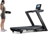 Woman using a NordicTrack treadmill with a screen displaying an instructor.