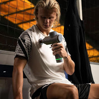 Person using a handheld massage device in front of a sports net