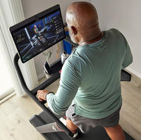 Man exercising on a treadmill with a screen displaying a workout program.