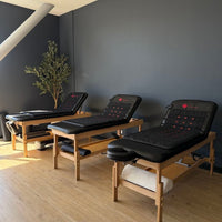 Three massage beds in a room with a dark wall and wooden floor.
