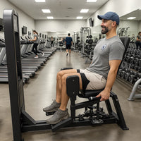 Man exercising on a machine in a gym with other equipment and people in the background